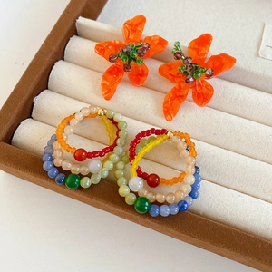 Detailed macro view of vintage orange glass flower earrings and colorful beaded rings