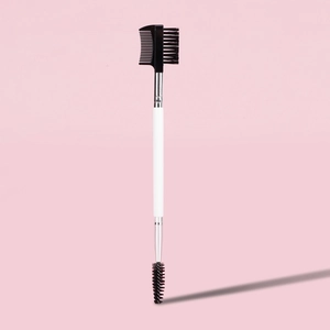 Close-up of a dual-ended eyebrow and eyelash brush with a white handle on pink background