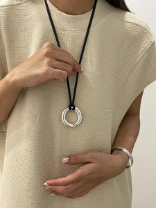 Close-up of a silver ring pendant on black cord necklace worn over beige knitwear
