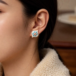 Macro shot of vintage enamel leaf earring with blue scrollwork and pink gemstone