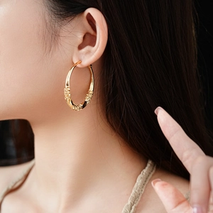 Detailed view of large gold twisted hoop earrings with embossed texture worn by a model