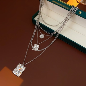 Close-up of layered silver necklaces with hammered square pendants in a green gift box