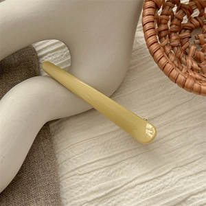 Detail of light yellow duckbill hair clip on textured beige fabric for styling