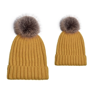 Detailed knit texture of two yellow beanies with fluffy faux fur pom poms for family