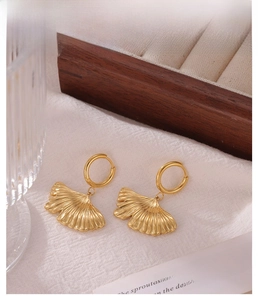 Macro detail of golden ginkgo leaf hoop earrings with intricate vein textures on a wood box