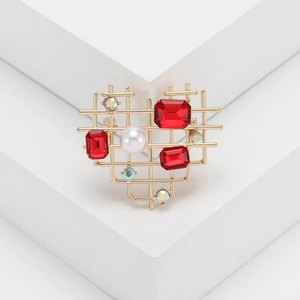 Hollow heart brooch in gold metal with red crystals and pearl on white geometric stands