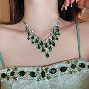 Close-up of V-shaped silver necklace with emerald cut green stones and tassel diamonds