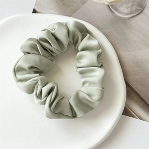 Détail d'un chouchou en satin vert sauge sur une assiette en céramique blanche élégante