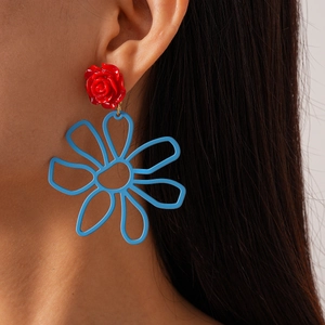 Détail de boucles d'oreilles rose rouge et fleur bleue ajourée sur l'oreille