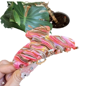 Pink marble texture acetate hair claw clip for women held against a leaf background