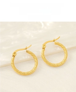Detail of gold geometric hoop earrings with twisted rope texture on white silk fabric