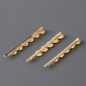 Close-up of three golden wave-shaped metal hair clips displayed on a gray background