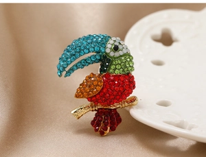Detailed close-up of a colorful parrot brooch with rhinestones on a beige fabric surface