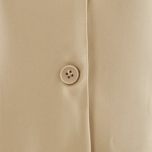 Close-up of beige woven fabric texture and matching four-hole button on the cardigan