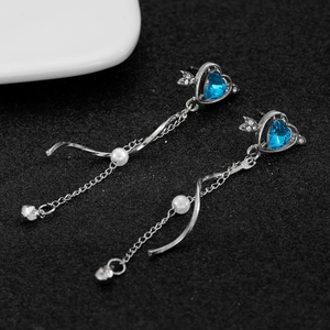 Detailed macro view of silver tassel earrings featuring blue heart stone and white pearl