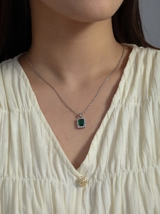 Close-up of elegant silver necklace featuring a rectangular green gemstone pendant with zircons