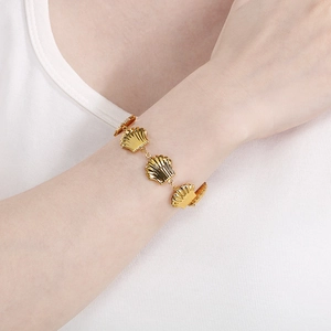 Detailed view of a gold-plated stainless steel bracelet with shell charms on a wrist