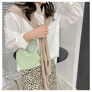 Mint green heart-shaped jelly bag with gold chain strap worn by a model in a casual setting