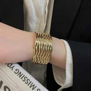 Nahaufnahme eines breiten gewellten goldenen Armreifs mit glänzender Metallstruktur.