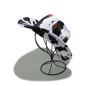 Detailed close-up of cow print western cowboy hat with curved brim on metal stand