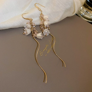 Détail de boucles d'oreilles muguet avec pétales blancs et longues pampilles en chaîne or