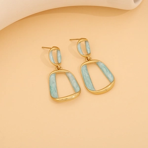Detail of geometric stainless steel earrings with gold frames and light blue marble resin