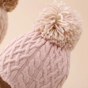 Detailed close-up of pink knit baby hat featuring thick cable weave and bicolor pom-pom