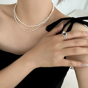 Close-up of double-layer white beaded necklace and silver ring with heart black stone