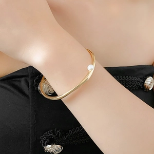 Detailed view of a gold geometric cuff bracelet with a single pearl on a female wrist