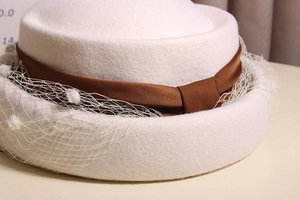 Detail of wool beret with mesh veil, ribbon bow, and soft textured fabric in cream white