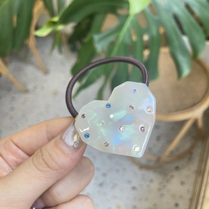 Pearly heart hair tie with colorful rhinestones held against a natural green background