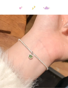 Close-up of a delicate silver bracelet featuring a small green gemstone pendant on wrist