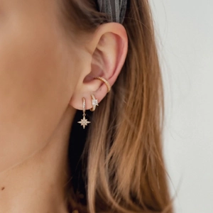 Close-up of gold-plated star pendant earring and zircon ear cuffs worn on model ear