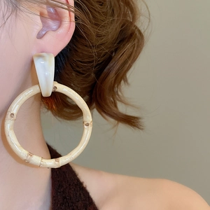 Close-up of model wearing geometric resin and bamboo hoop earrings in warm tones