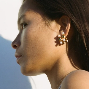 Detailed view of C-shaped gold-plated earrings with white pearls and green square gemstones