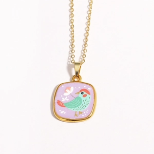 Close-up of gold enamel pendant featuring a green bird and purple background detail