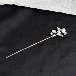 Detailed shot of silver ginkgo leaf hair pin with white pearls on a black background