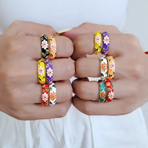 Macro detail of colorful daisy enamel rings set on fingers showing floral craft
