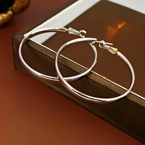 Détail des boucles d'oreilles créoles rondes en métal argenté sur surface en bois