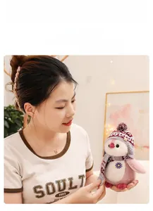 Pink penguin plush toy with knit scarf and hat held by a model in a cozy home setting