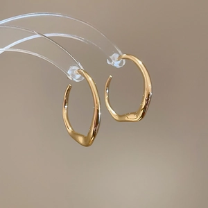 Macro shot of minimalist golden irregular twisted hoop earrings on an acrylic stand