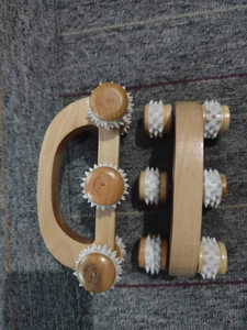 Detail eines Holzmassage-Rollers mit weißen Gummizahnrädern auf einer dunklen Oberfläche