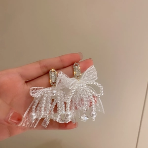 Detailed view of gold bow earrings with cascading lace, pearls, and crystals fringe