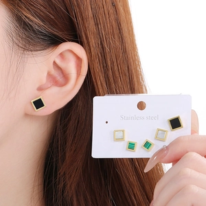 Detailed view of three pairs of minimalist square stud earrings in black, white and green