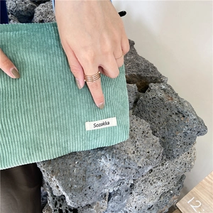 Close-up of light green corduroy makeup bag with textured fabric and woven logo label