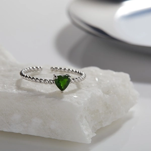 Macro shot of a heart-shaped green gemstone ring with a twisted silver band on stone