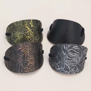 Detailed view of four vintage leather hair ties in dark green, black, bronze, and silver