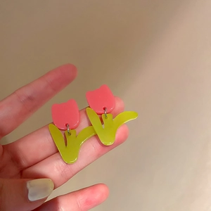 Gros plan de boucles d'oreilles tulipes roses et feuilles vert-jaune sous lumière douce