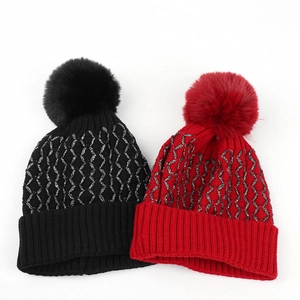 Detail of knit beanie featuring silver metallic thread pattern and faux fur pom-poms