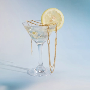 Dettaglio della collana a catena a graffetta dorata avvolta su un bicchiere da martini